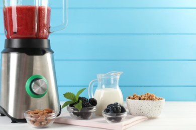 Photo of Blender with mixture of ingredients and other fresh products on white wooden table