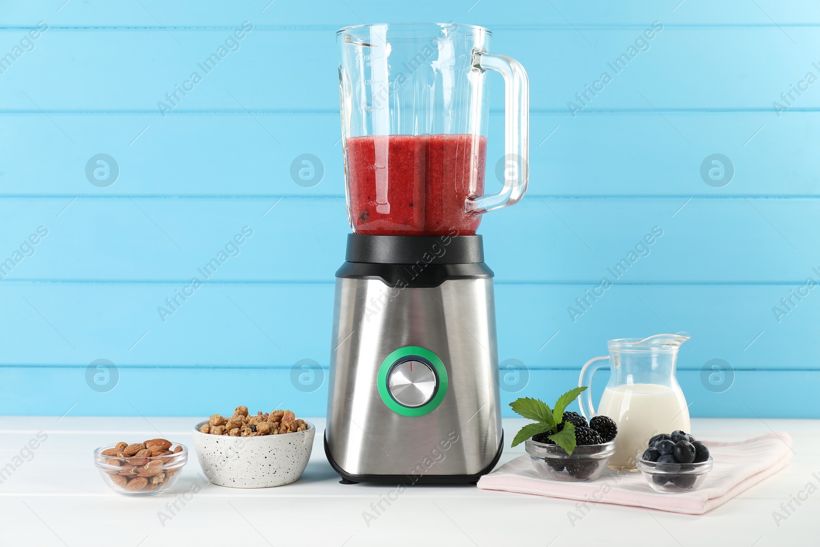 Photo of Blender with mixture of ingredients and other fresh products on white wooden table