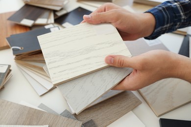 Photo of Man choosing wooden flooring among different samples at table, closeup