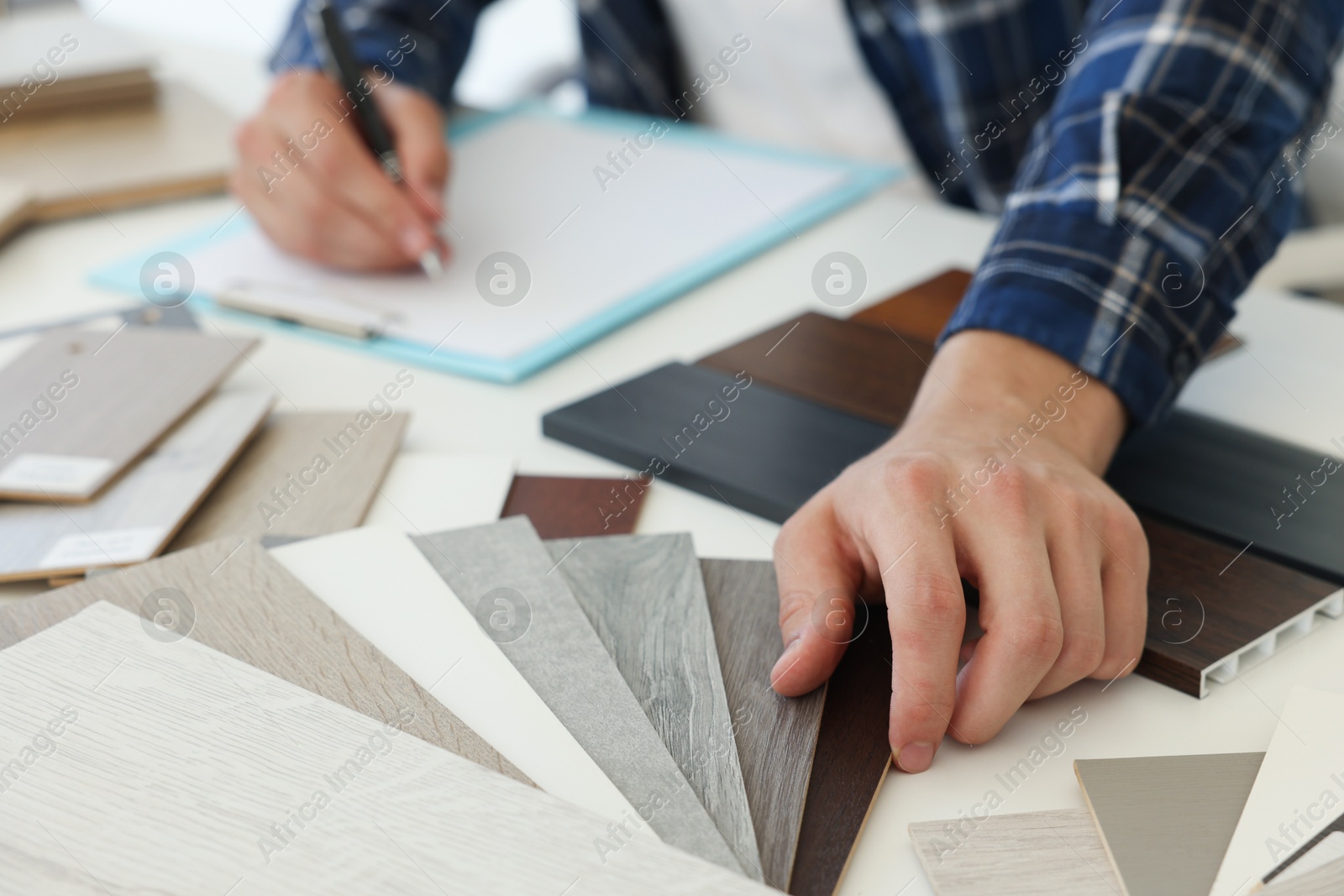 Photo of Man taking notes at table with different samples of wooden flooring indoors, closeup