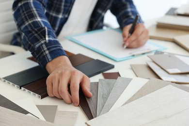 Photo of Man taking notes at table with different samples of wooden flooring indoors, closeup