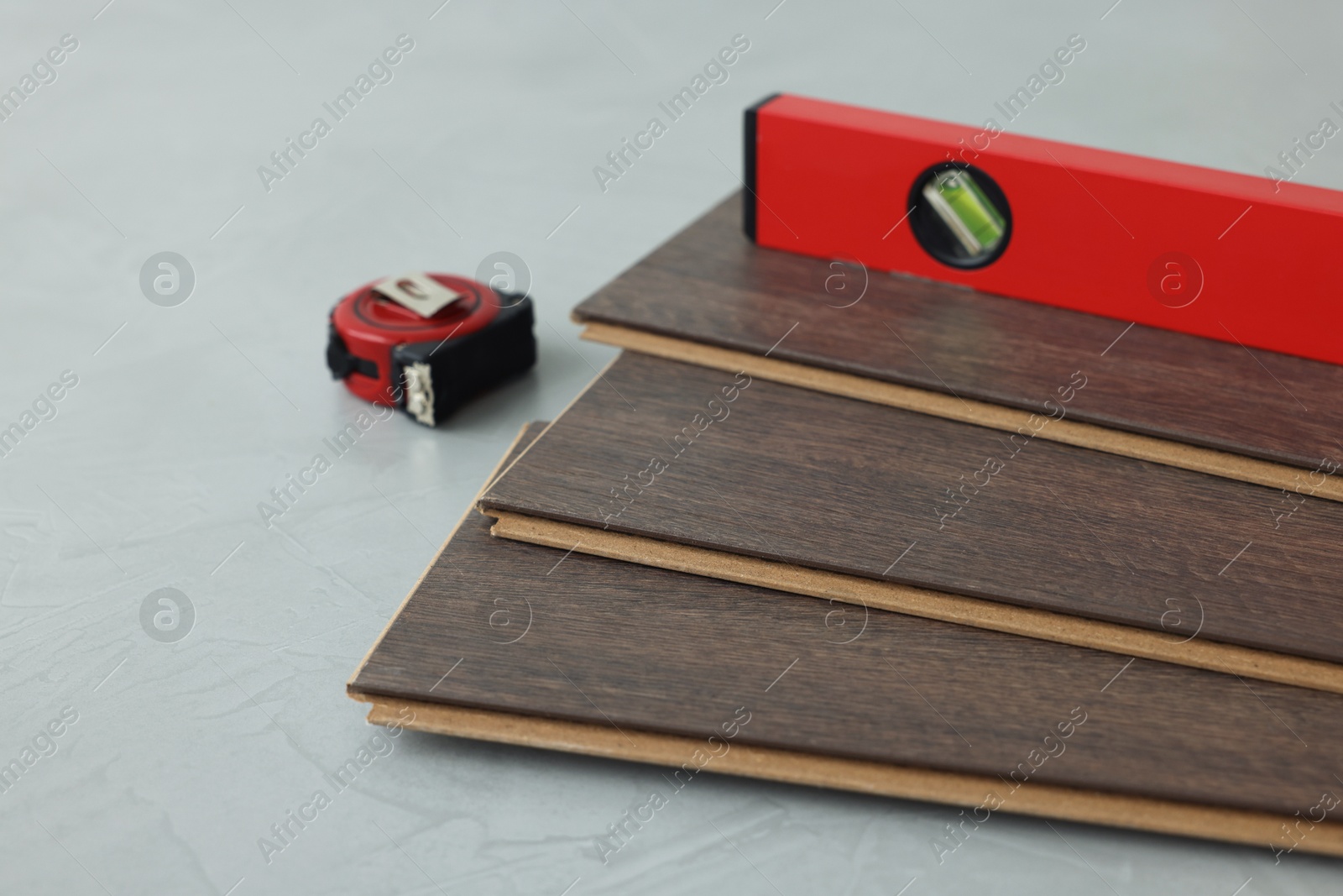 Photo of Measuring tape, level tool and laminate flooring pieces on grey textured surface, closeup