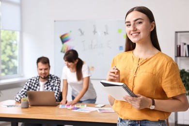 Happy young designer with notebook in office