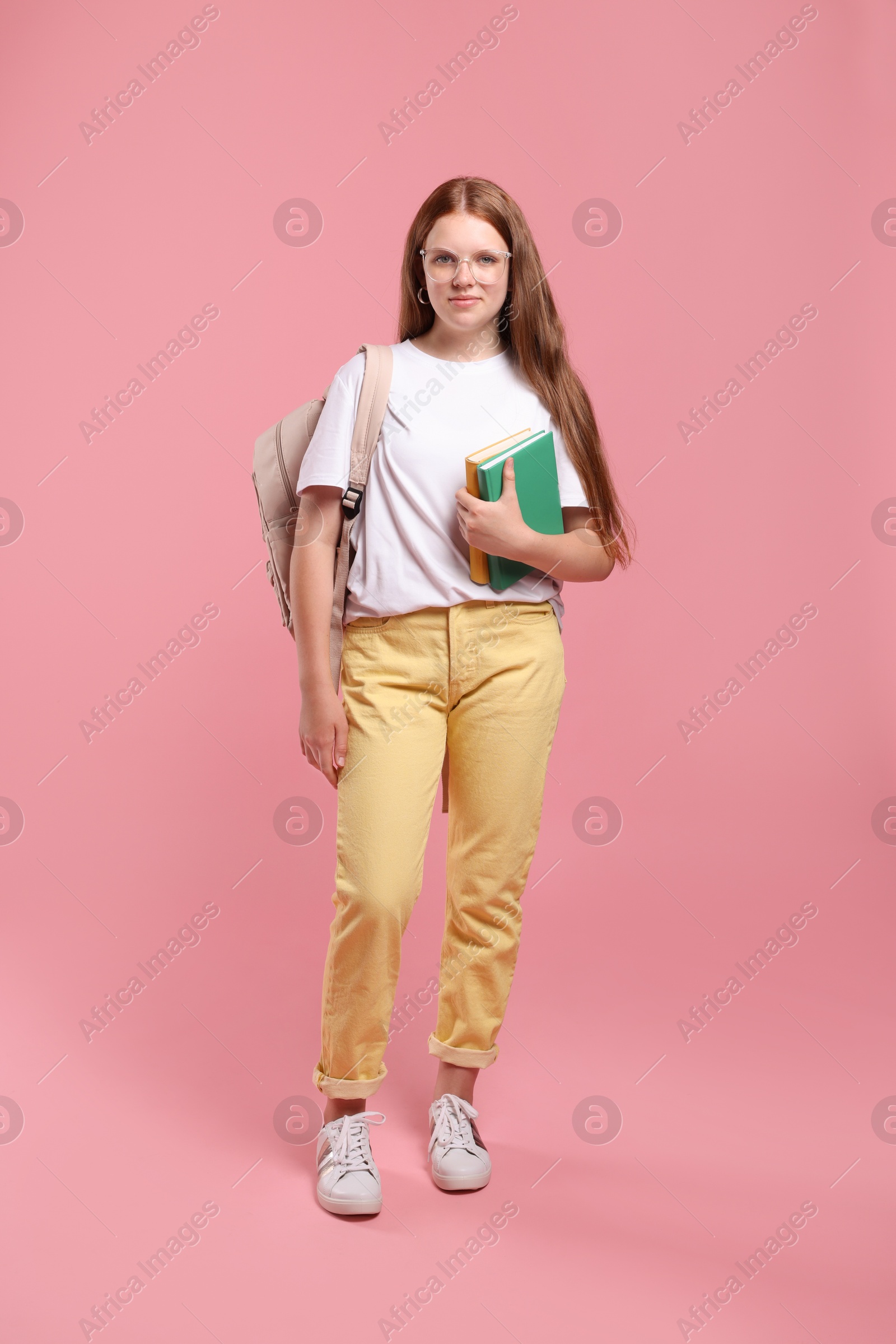 Photo of Teenage girl with backpack and books on pink background