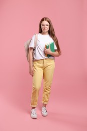 Teenage girl with backpack and books on pink background