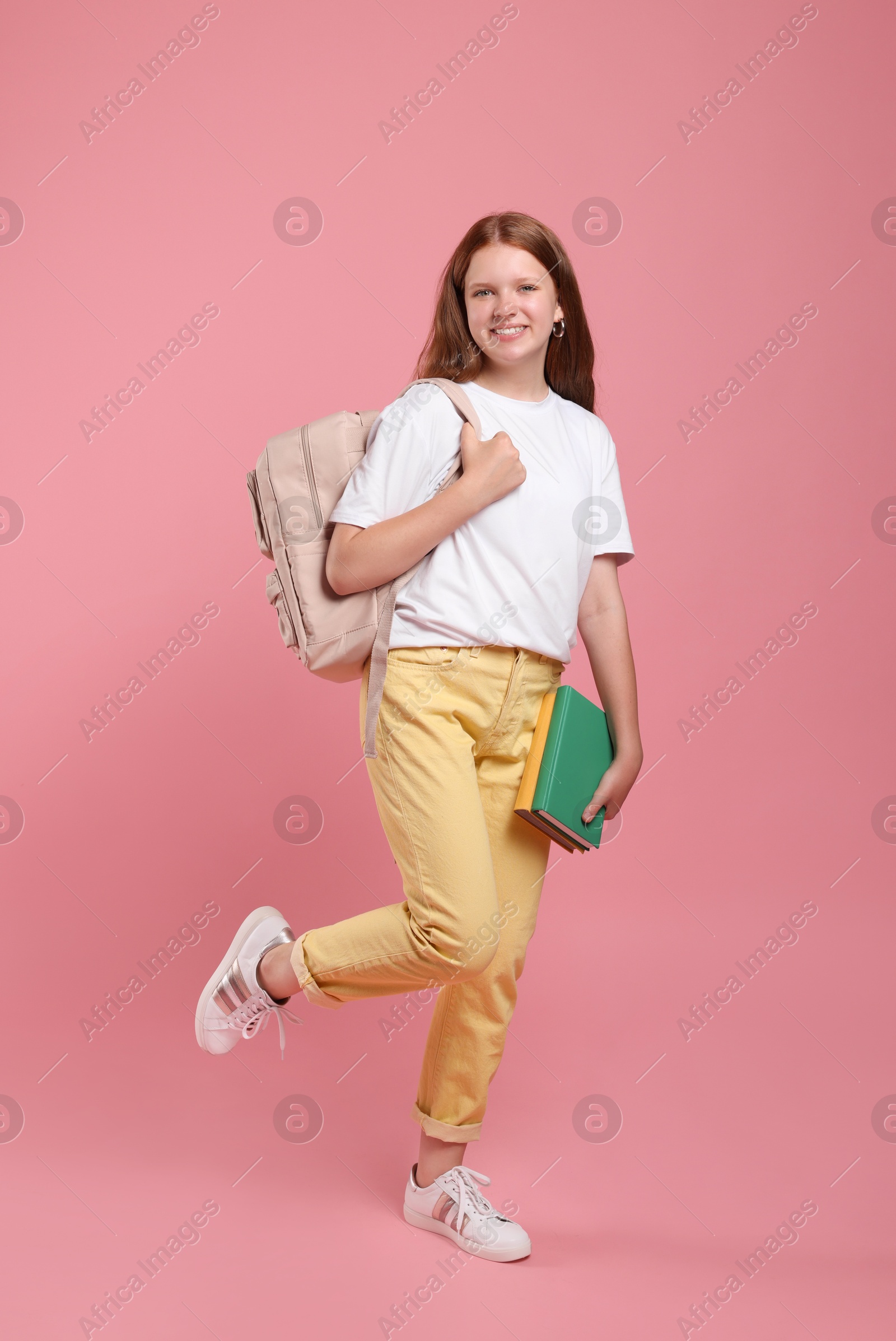 Photo of Teenage girl with backpack and books on pink background