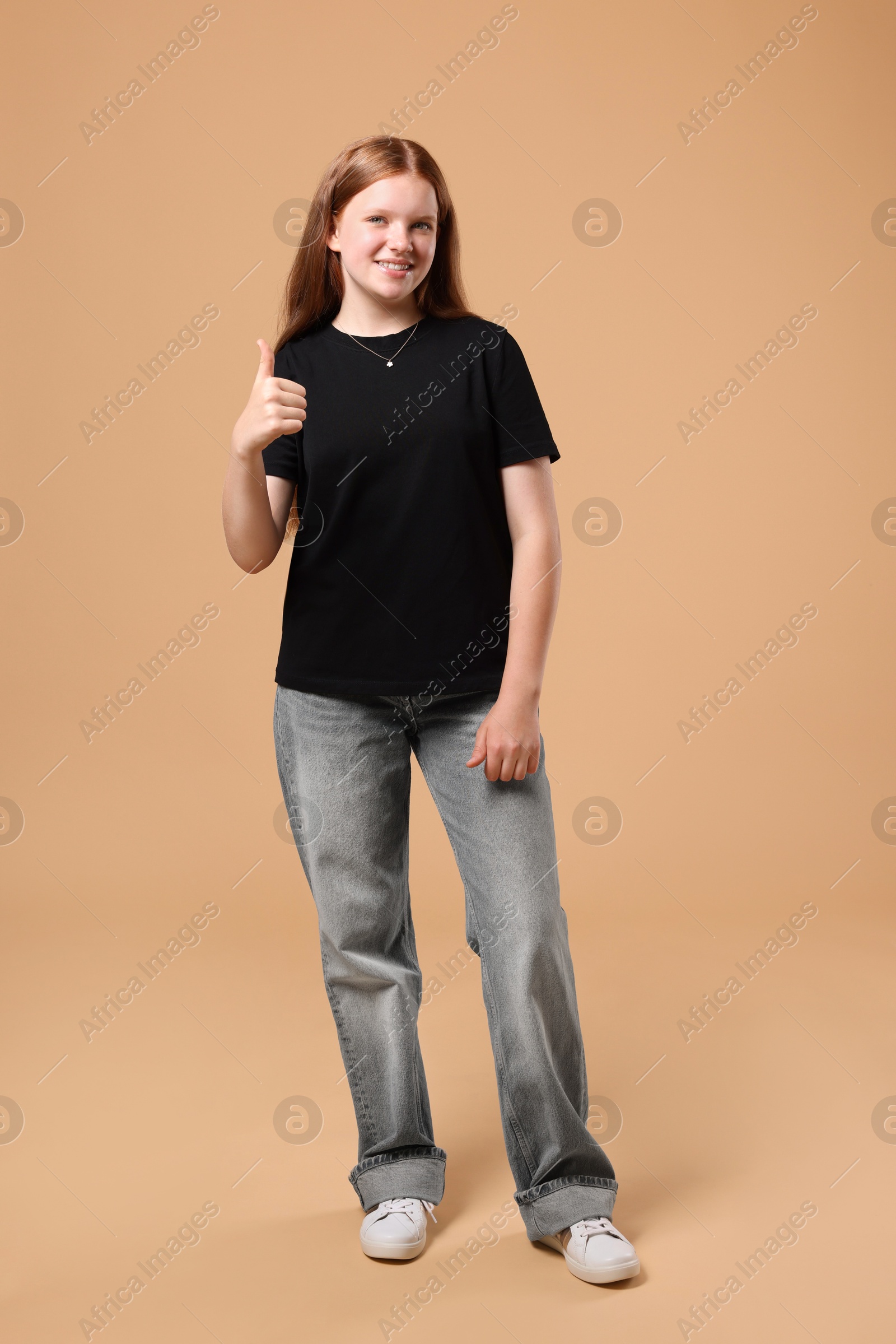 Photo of Teenage girl showing thumbs up on beige background