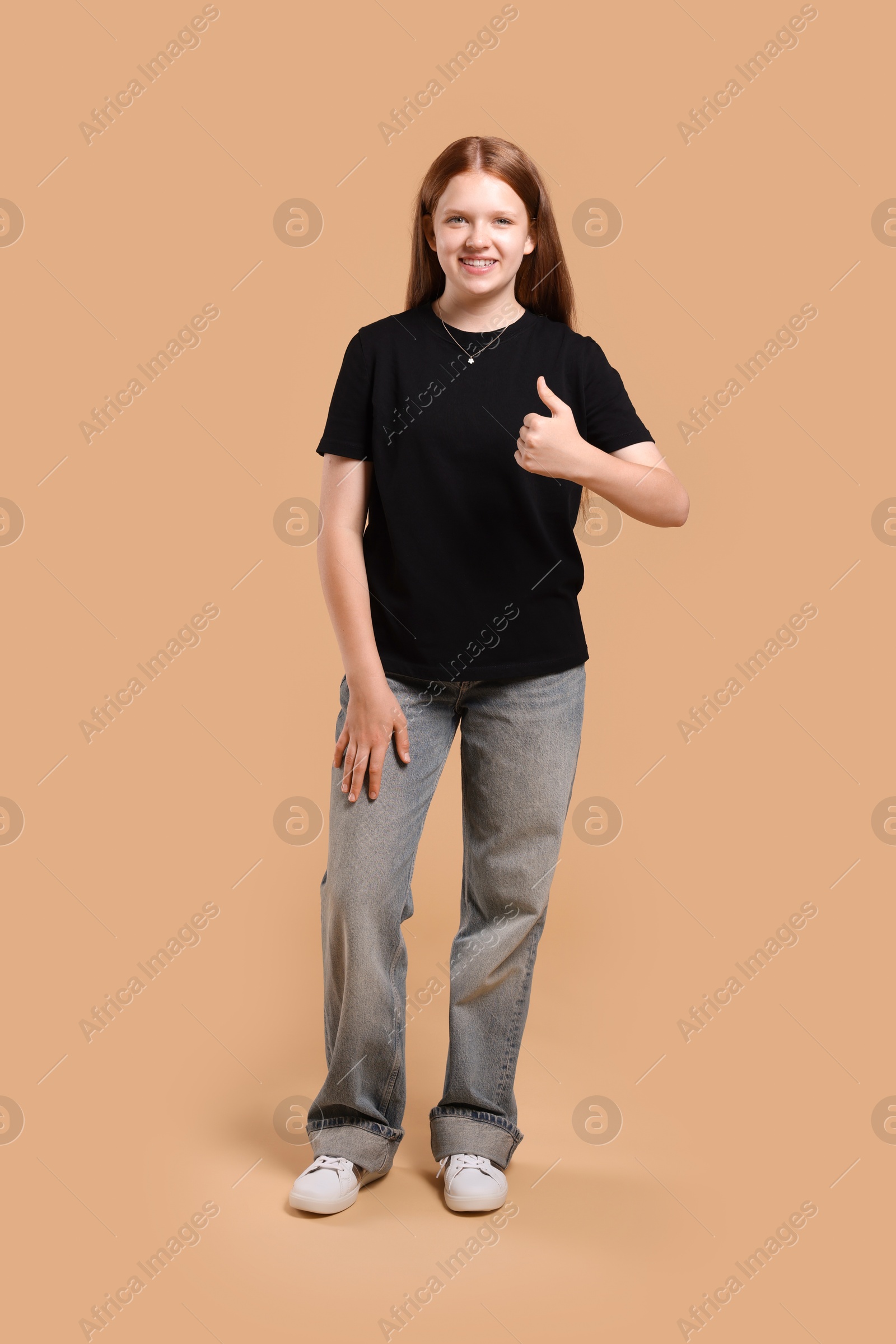 Photo of Teenage girl showing thumbs up on beige background