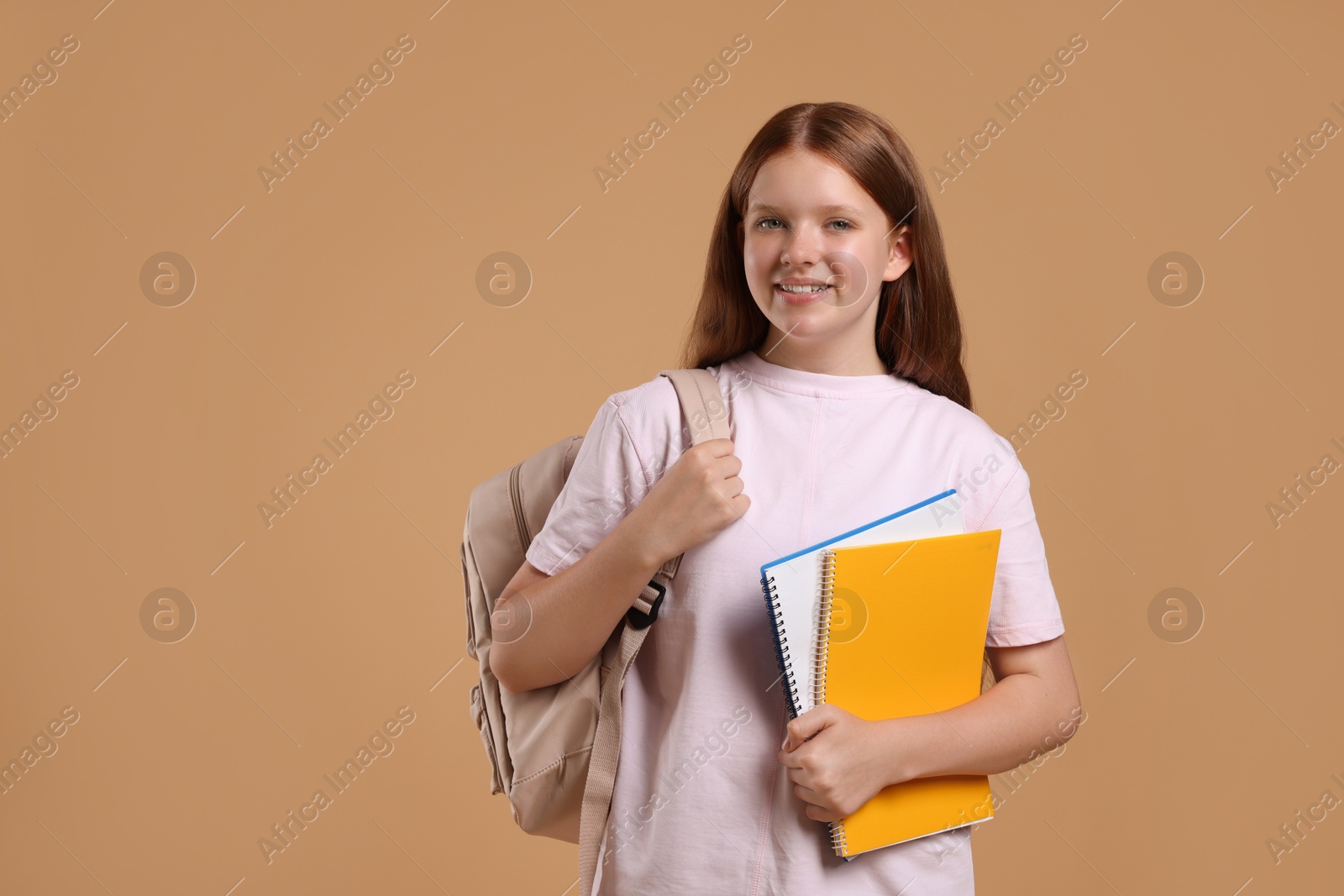 Photo of Teenage girl with backpack and books on beige background, space for text