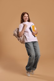 Teenage girl with backpack and books on beige background