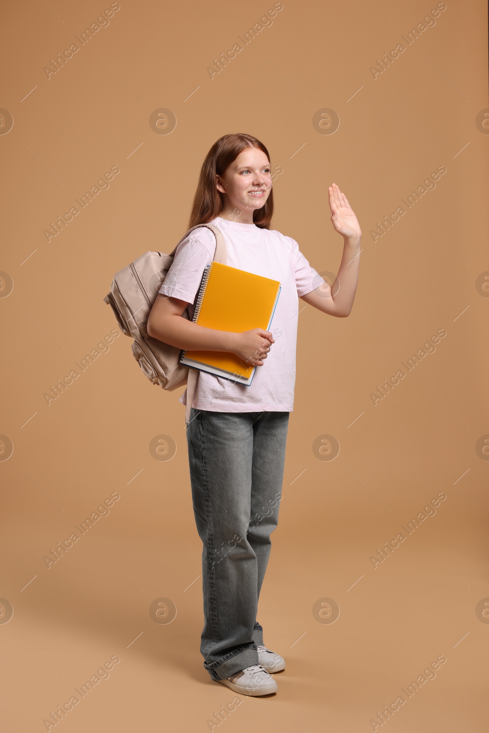 Photo of Teenage girl with backpack and books on beige background