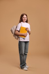 Teenage girl with backpack and books on beige background