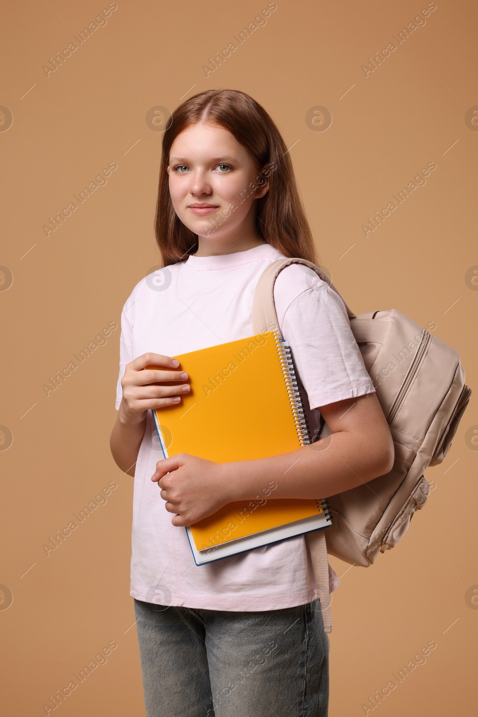 Photo of Teenage girl with backpack and books on beige background