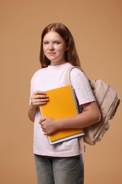 Teenage girl with backpack and books on beige background