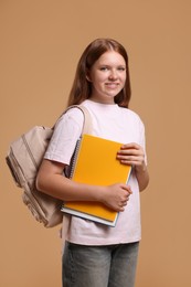 Photo of Teenage girl with backpack and books on beige background