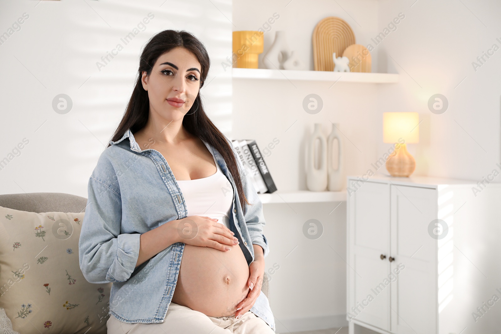 Photo of Young pregnant woman sitting on sofa at home, space for text