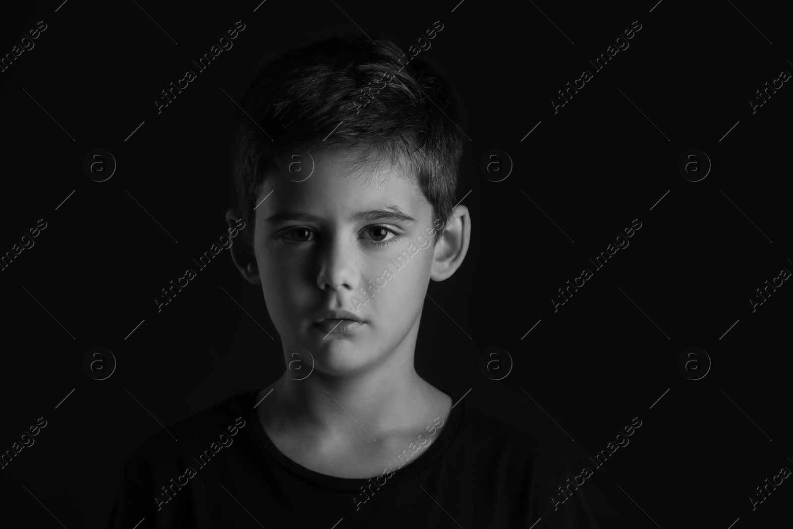 Photo of Portrait of sad little boy on dark background. Black and white effect