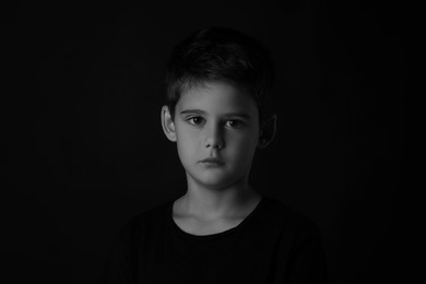 Photo of Portrait of sad little boy on dark background. Black and white effect