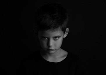 Photo of Angry little boy on dark background. Black and white effect