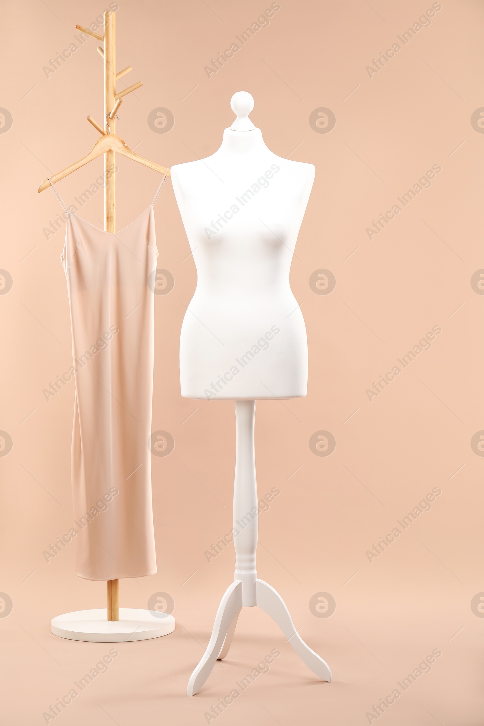 Photo of One female mannequin on stand and rack with dress against beige background