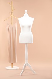 One female mannequin on stand and rack with dress against beige background