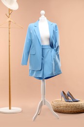 Photo of One female mannequin with shorts and jacket, rack, pouf and shoes against beige background