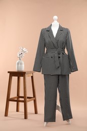 Female mannequin with suit, stool and cotton flowers on beige background