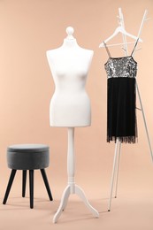 Photo of One female mannequin, rack, dress and ottoman on beige background