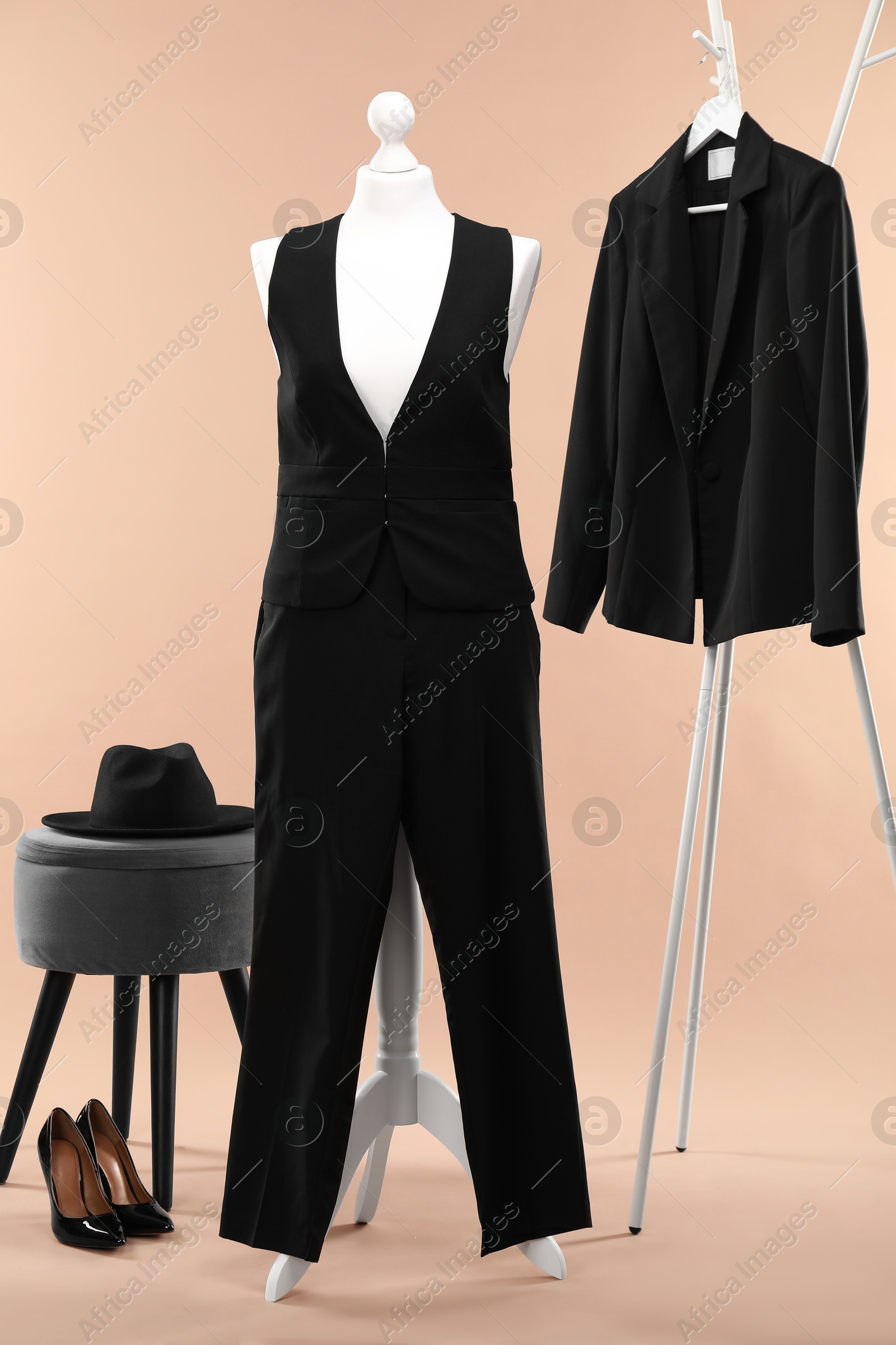 Photo of Female mannequin with suit, ottoman, hat, rack, jacket and shoes on beige background