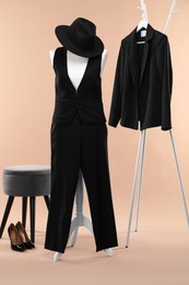 Photo of Female mannequin with suit, hat, ottoman, rack, jacket and shoes on beige background