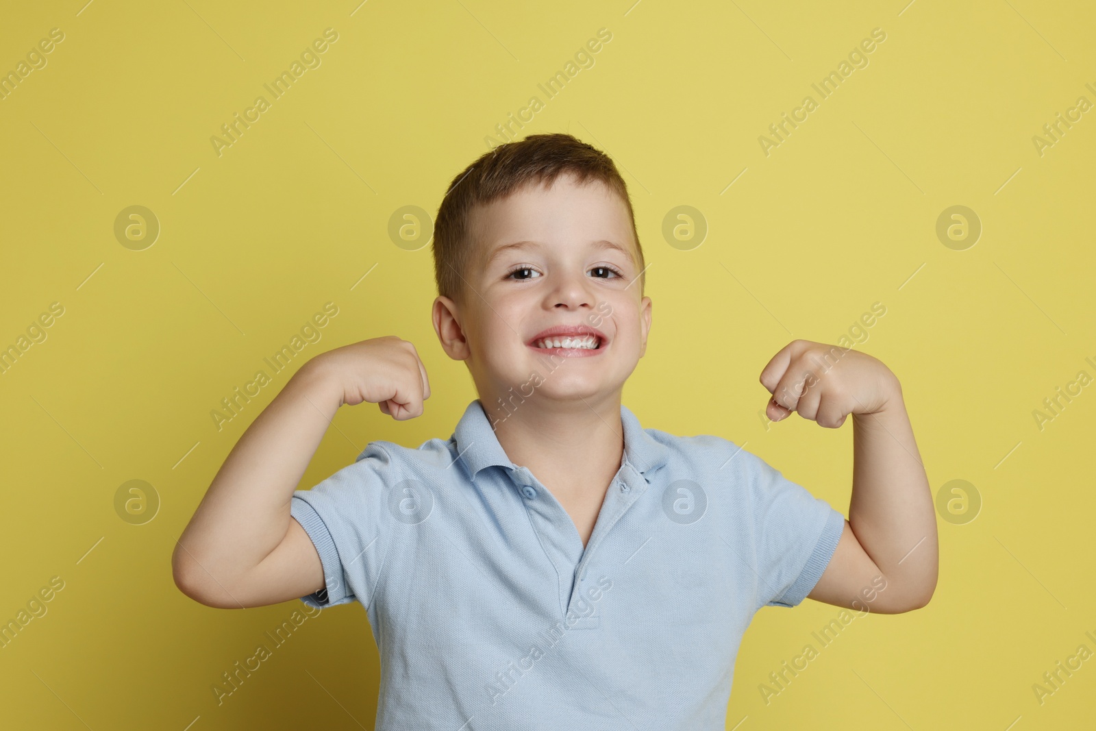 Photo of Cute little boy showing his biceps on yellow background