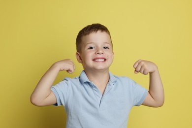 Photo of Cute little boy showing his biceps on yellow background