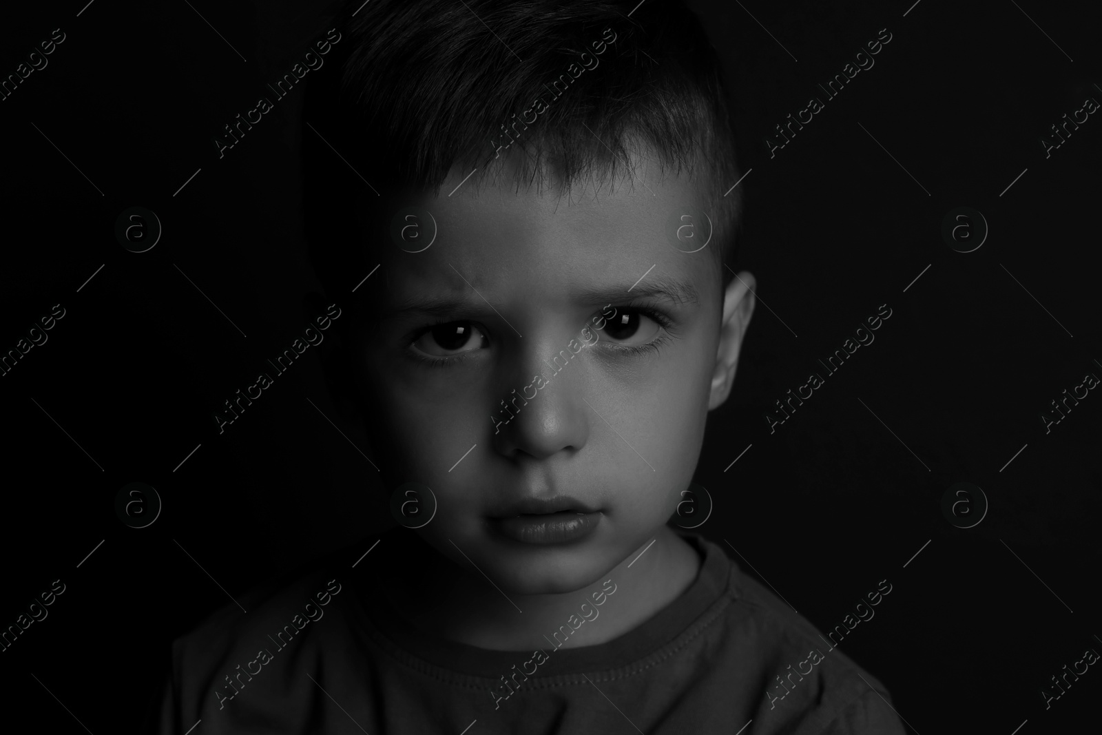 Photo of Portrait of sad little boy on dark background. Black and white effect