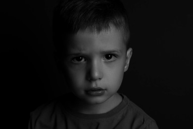 Photo of Portrait of sad little boy on dark background. Black and white effect