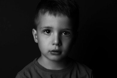 Portrait of sad little boy on dark background. Black and white effect