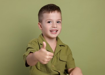 Cute little boy showing thumbs up on green background