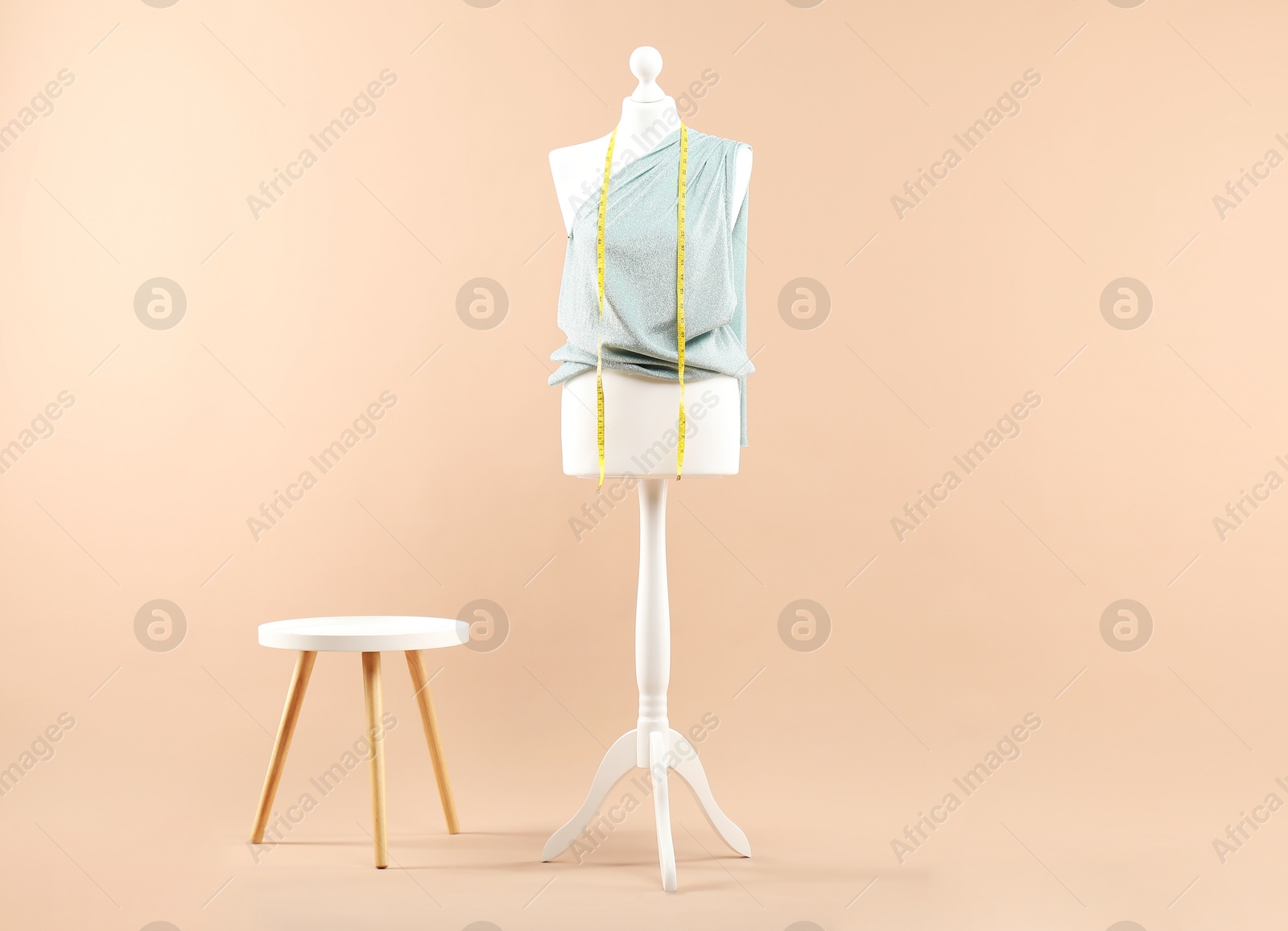 Photo of Mannequin with cloth, measuring tape and stool on beige background