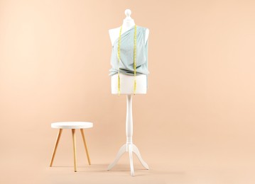 Mannequin with cloth, measuring tape and stool on beige background