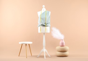 Mannequin with cloth, measuring tape, vase and stool on beige background