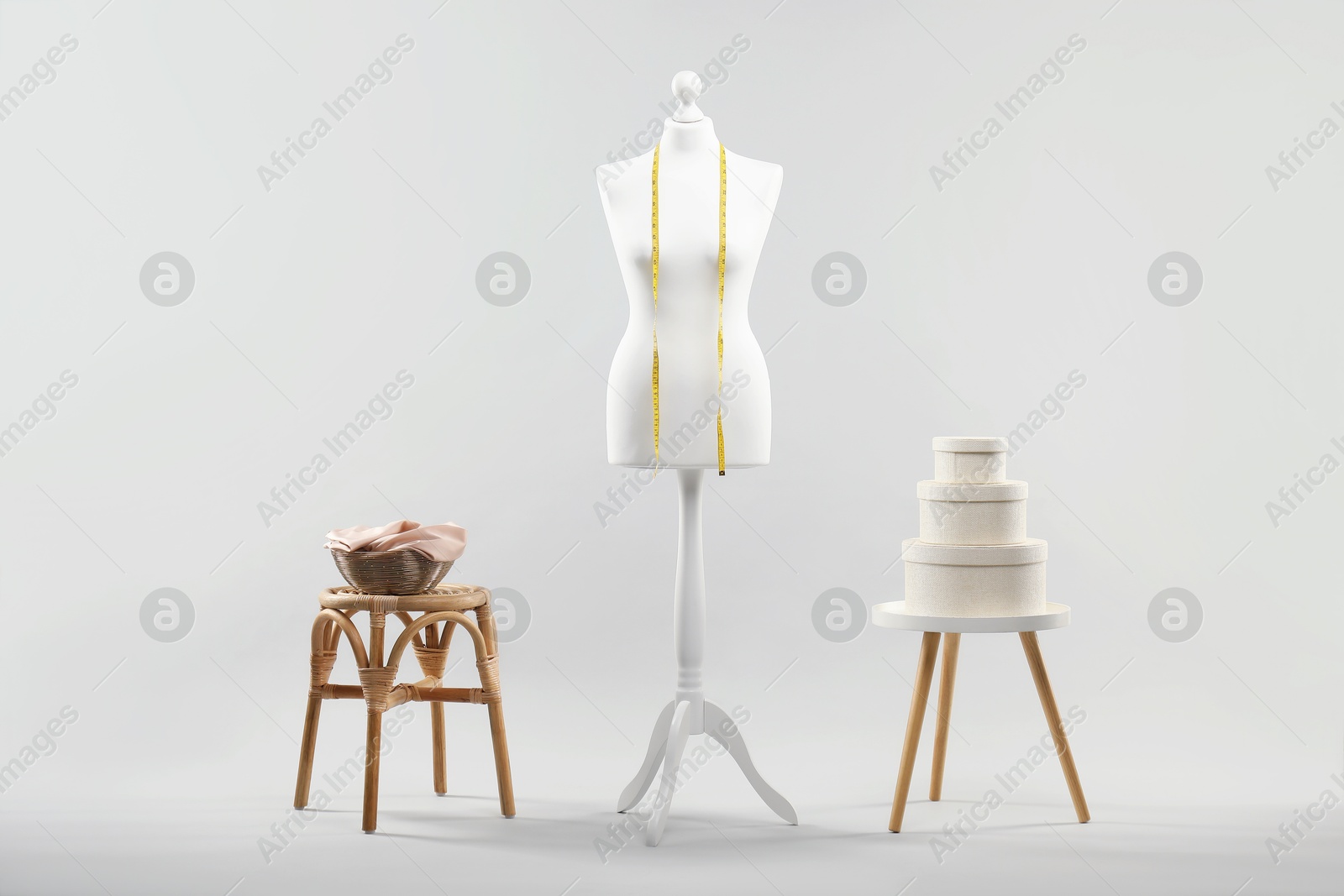 Photo of Mannequin with measuring tape and stools on light grey background