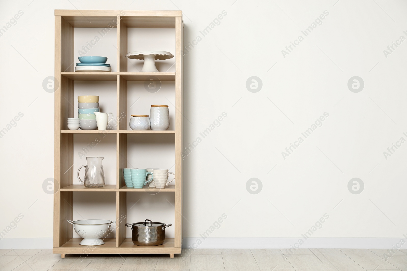 Photo of Wooden shelving unit with kitchenware near white wall indoors, space for text