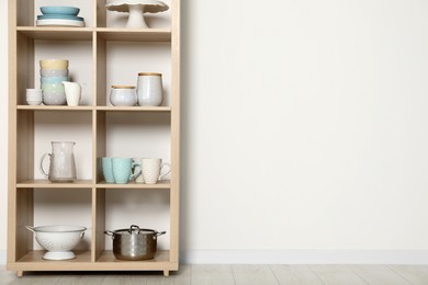 Wooden shelving unit with kitchenware near white wall indoors, space for text