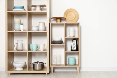 Photo of Wooden shelving units with kitchenware near white wall indoors