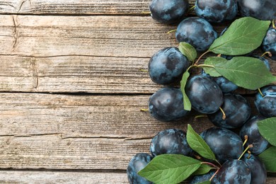 Photo of Tasty ripe plums and leaves on wooden table, flat lay. Space for text