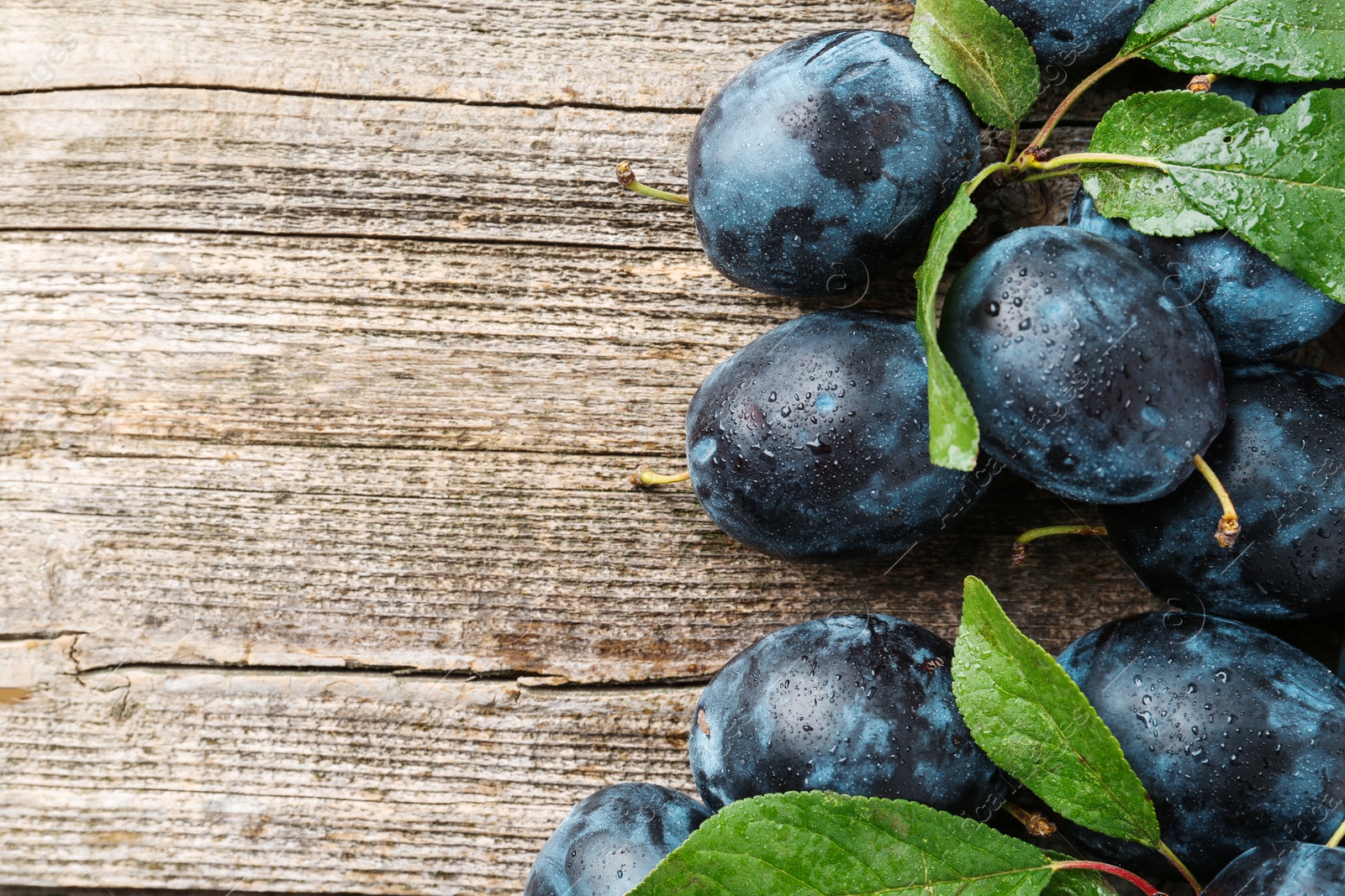 Photo of Tasty ripe plums and leaves on wooden table, flat lay. Space for text