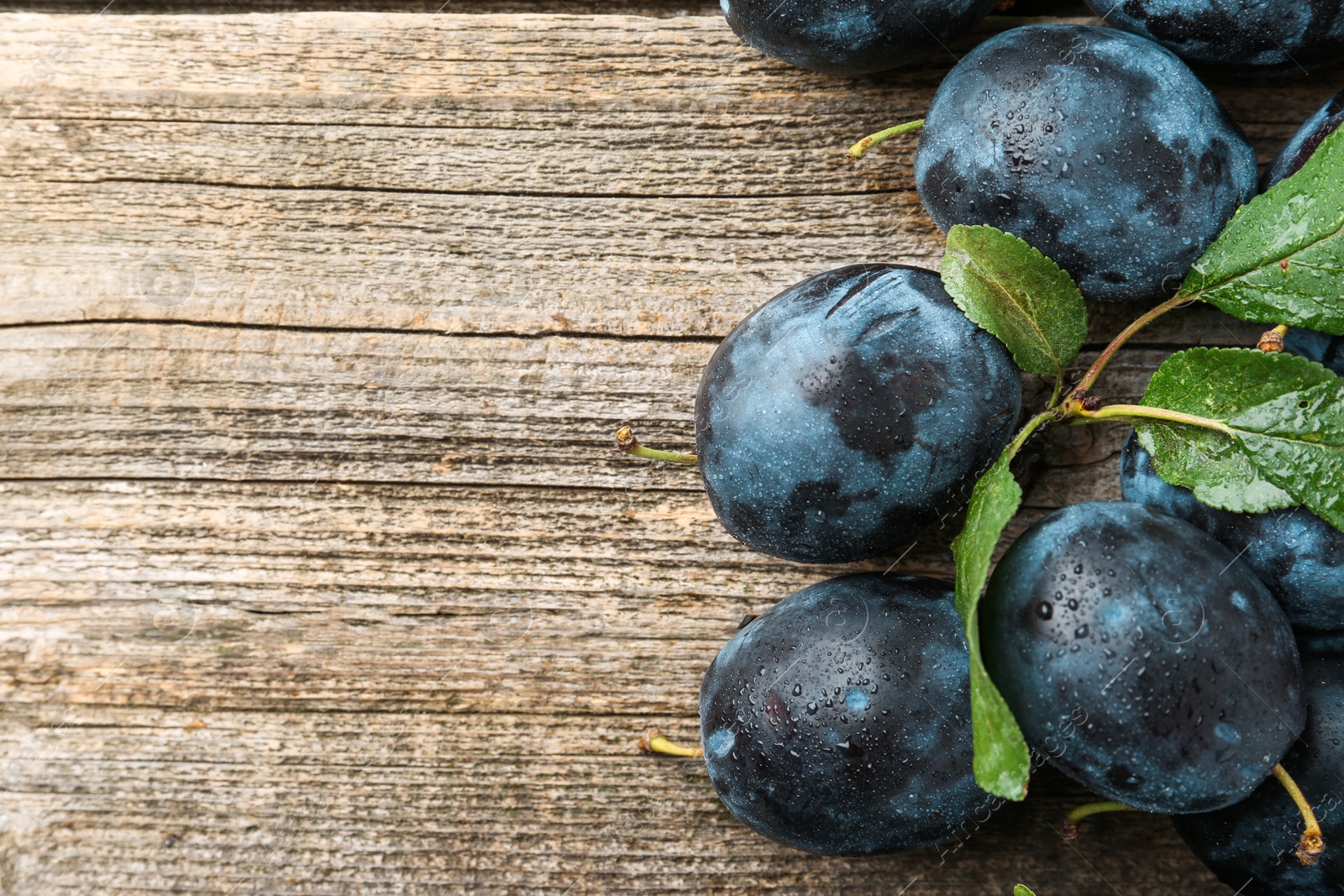 Photo of Tasty ripe plums and leaves on wooden table, flat lay. Space for text