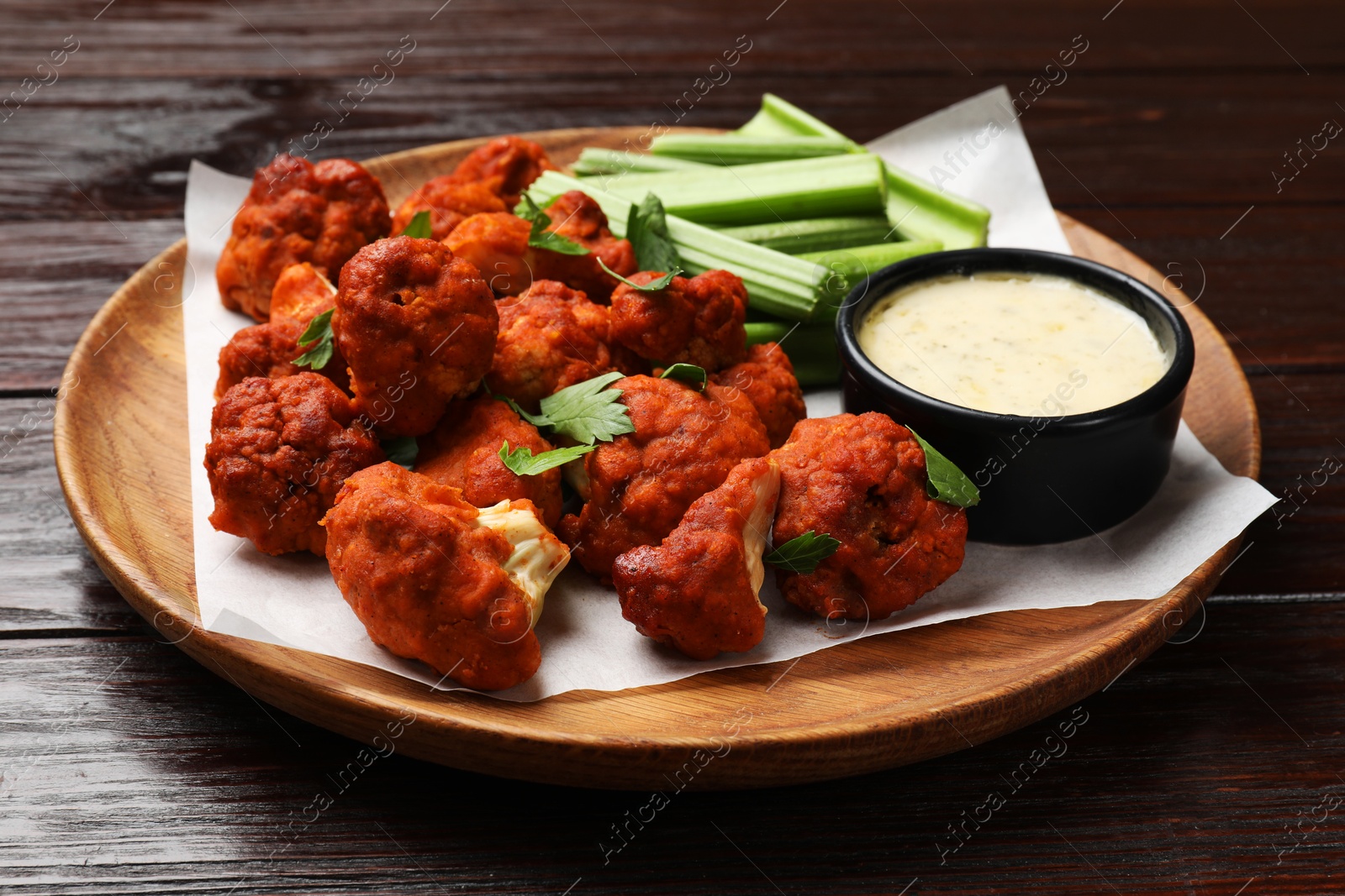 Photo of Baked cauliflower buffalo wings with celery and sauce on wooden table, closeup