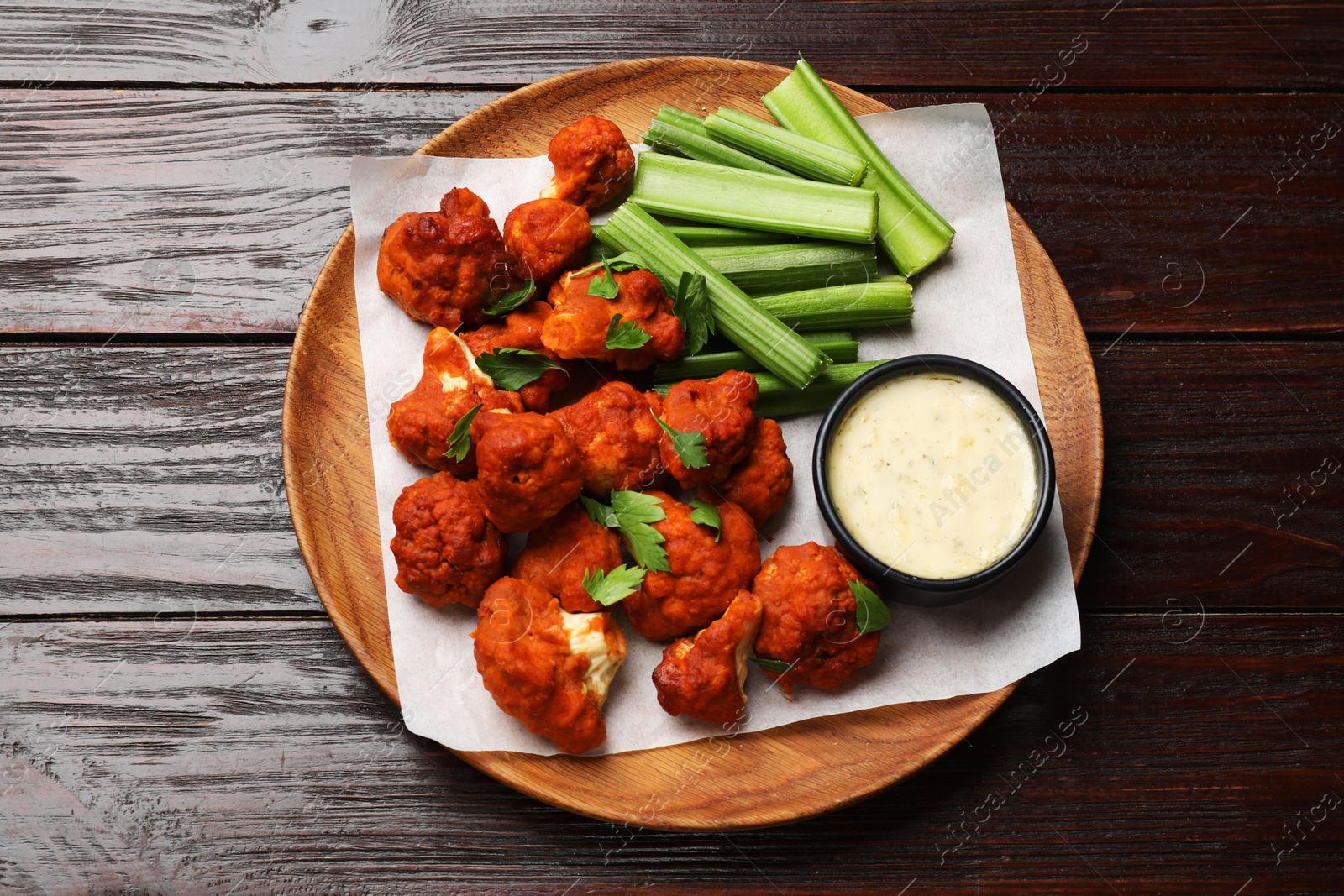 Photo of Baked cauliflower buffalo wings with celery and sauce on wooden table, top view