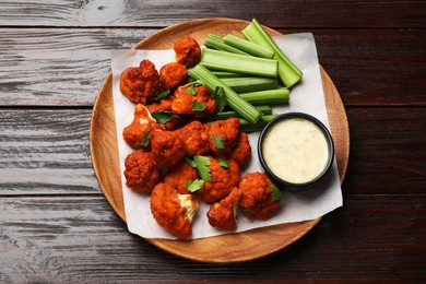 Photo of Baked cauliflower buffalo wings with celery and sauce on wooden table, top view