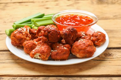 Photo of Tasty cauliflower buffalo wings, sauce and celery on wooden table, closeup